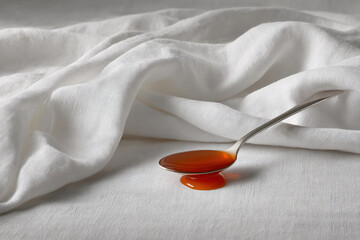 single drop of honey elegantly rests on gleaming spoon surrounded by soft linen backdrop