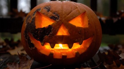 Spooky carved pumpkin with a flickering candle inside displayed outdoors among fallen autumn leaves ready for Halloween.