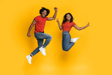A joyful young couple is jumping in excitement against a bright yellow background. They are wearing matching red shirts and denim jeans, showcasing their playful energy and connection.