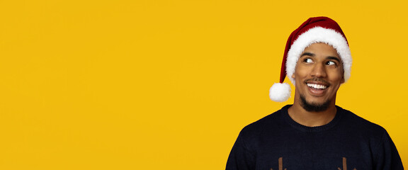 A cheerful man with a big smile is wearing a Santa hat and a festive sweater. The vibrant yellow background adds to the joyful holiday spirit. This scene captures winter celebrations and happiness.