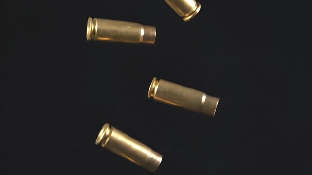 Realistic slow motion shot of spent brass bullet casings falling and tumbling against an isolated black background