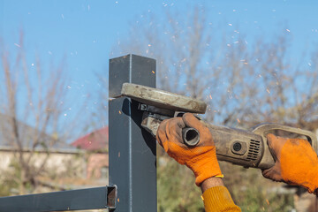 A worker cuts a metal pole with a power grinder. The man uses a hand-held circular saw.