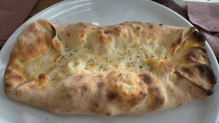 Calzone pizza on a white plate covered with cheese