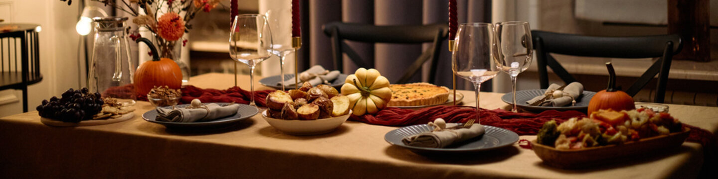 Header of Thanksgiving dinner table set with pumpkin pie, roasted vegetables, assorted gourds, wine glasses, plates, napkins, festive centerpiece, no people visible, indoor setting
