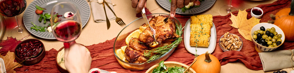 Header of diverse group of young and middle aged friends sharing Thanksgiving dinner, hands of multiethnic men and women serving roast turkey, passing food, holding wine glasses, enjoying festive meal