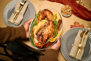 Male hands holding roasted turkey garnished with orange slices and herbs, serving Thanksgiving...