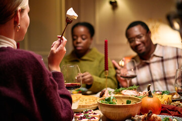 Diverse group of young adult and middle aged friends sharing Thanksgiving dinner, Caucasian woman holding fork with dessert in foreground, Black man and woman enjoying meal together