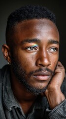 Obraz premium A young man looks away, hand near his face, with a rainbow reflection on his eye in a studio