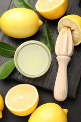 Fresh lemon juice, fruits and squeezer on black wooden table, flat lay