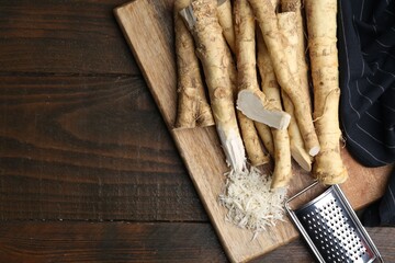 Grated horseradish, grater and fresh roots on wooden table, top view. Space for text