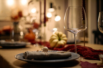 Closeup of elegant table setting with empty wine glass, ceramic plate, cloth napkin and decorative pumpkin on festive dining table prepared for Thanksgiving dinner among friends