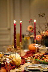 Thanksgiving dinner table set with roasted turkey, pumpkins, burning red candles, glassware and autumn floral arrangements, festive meal prepared for gathering among friends