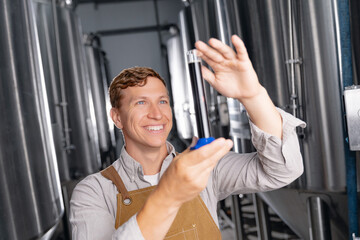 Young caucasian male brewer inspecting liquid sample in brewery facility. Concept drink industry with quality product for craft beer