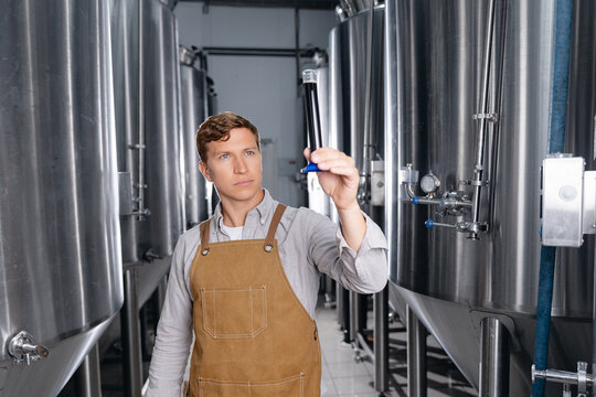 Young caucasian male brewer inspecting beer quality in modern brewery. Concept drink industry with quality product