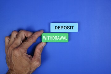 A hand holds a green block labeled “WITHDRAWAL” beside a blue block labeled “DEPOSIT,” representing banking transactions And Finance Concepts. with an blue background.