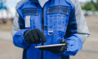 Worker using online tablet at shipyard cargo port in blue protective gear