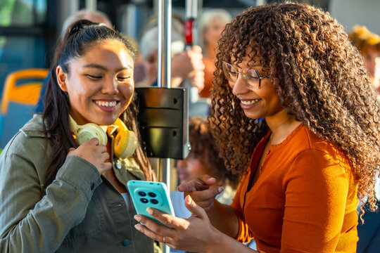 Diverse women friends sharing smartphone on bus