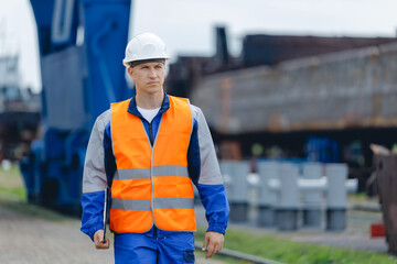 Young man industrial engineer in white hard hat and blue uniform use tablet. Concept inspector work in container terminal or cargo logistic center