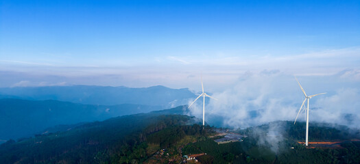 Wind generators with fog and clouds in mountains of Vietnam, industry landscape. Banner Turbines for eco renewable electric power production