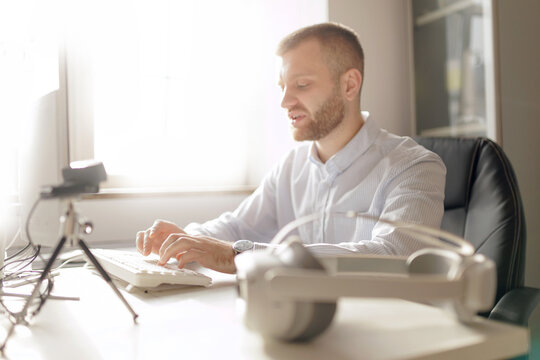 Portrait male adult typing at desk with vr headset in bright office setting, sunlight.