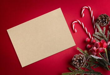 Christmas red background with blank paper, poinsettia, decorative fir branch, candy canes and cones for tree decoraton. New Year winter holiday composition with decor and copy space, top view.