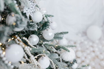 Christmas tree decorated with white and transparent balls made of eco-friendly material in the interior of a residential building against a white wall and fabric.