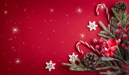 Christmas red background with decorative poinsettia, fir branch and snowflakes, candy canes and cones for tree decoraton. Winter holiday composition with decor and copy space, top view.