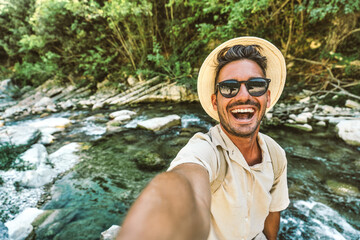Happy man taking selfie on jungle river background - Smiling hiker having fun on adventure trip - Technology life style concept
