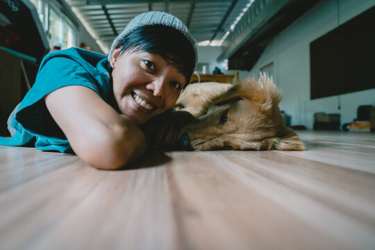 A real Asian man takes a selfie with a year-old golden retriever. The dog is licking its owner's face. Smiling People and fun playing together looking happily at the camera at home Pet and person