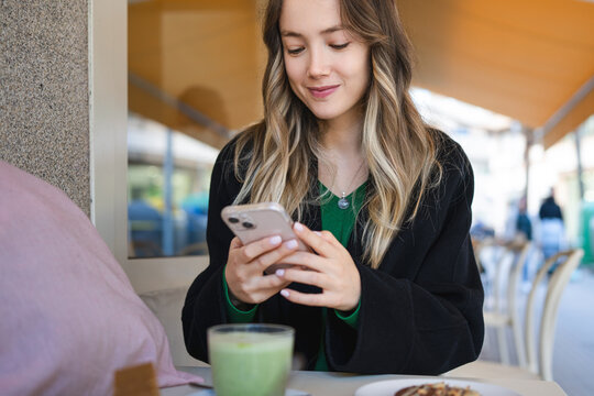 Woman using smartphone checking social media at cafe - Powered by Adobe