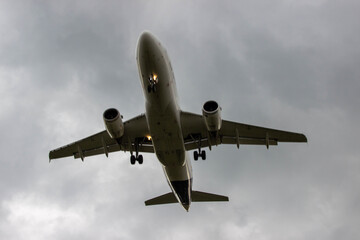 Airplane flying through cloudy sky, captured from below, showcasing landing gear and wings, illustrating aviation technology and travel experience with dramatic atmosphere