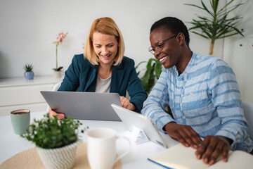 Diverse women collaborating on laptop and smiling at work