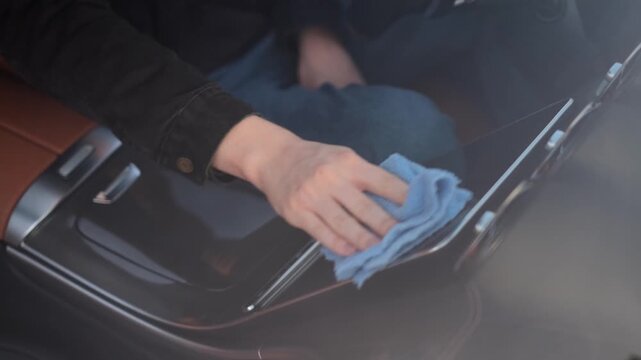 A driver wipes the digital screen in a car with a special cloth.