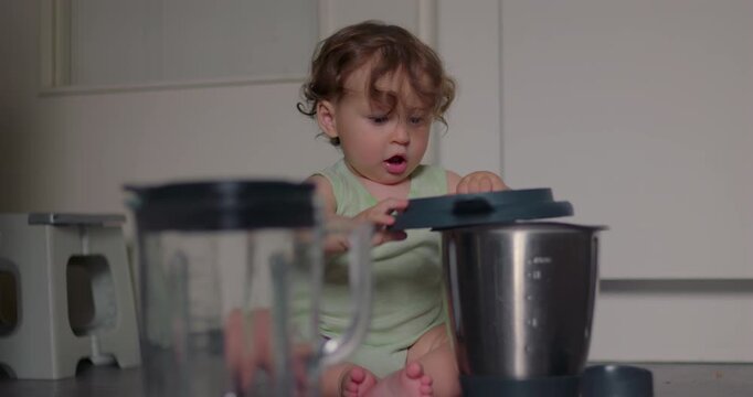 Curious toddler exploring kitchen container on the floor, gently tapping the lid with focused attention while sitting in bright home space surrounded by everyday household items