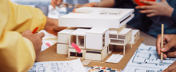 A dynamic architectural design session where a diverse group of designers collaborate around a model and blueprints, sharing ideas and creativity. SACTR