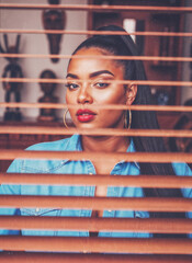 Editorial Portrait of Stylish Woman Behind Venetian Blinds in Urban Chic Setting, Featuring Vivid Blue Denim, Gold Hoop Earrings, Sultry Sunset-Reverie Color Grade and Cinematic Low-Key Lighting