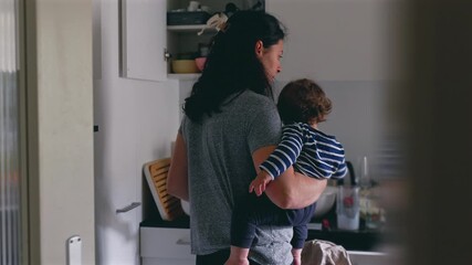 Mother holding toddler in quiet kitchen while preparing meal, creating tender everyday moment filled with calm connection, gentle presence, and comforting family routine at home