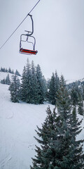 Ski lift chair above snowy pine forest in cold winter mountains