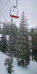 Empty ski lift chair gliding above frosted pine trees on a snowy mountain slope under a pale winter sky, capturing a quiet alpine atmosphere.