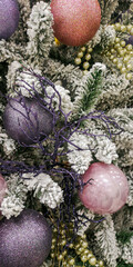 Festive Christmas tree decorated with pink, gold, and purple baubles on snowy pine branches creating a cozy holiday mood. Selective focus