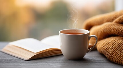 Warm cup of tea placed on wooden table beside an open book and cozy knitted sweater, creating a serene atmosphere for relaxation and contemplation