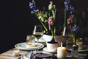 Spring elegant wedding or Easter celebration table decor. Festive white china, floral decoration with blooming bulbous hyacinth. Dark background. Springtime home gardening