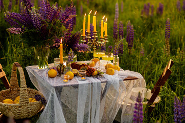 Beautiful romantic outdoor wedding decor. Table decorated with purple lupines flowers, lemons. Wineglasses with limoncello. Sunset, summer, golden hour. Perfect surprise date for loving couple