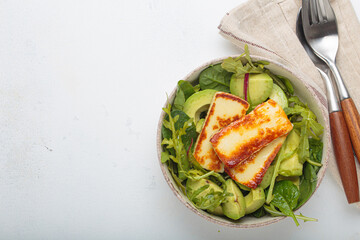 Fried halloumi cheese and sliced avocado salad with mixed green leaves, healthy and gourmet vegetarian meal, white background space for text
