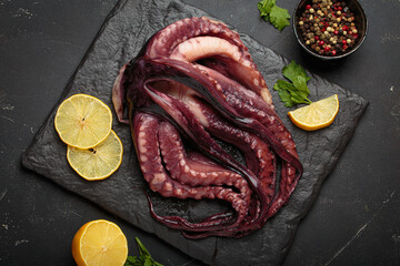 Raw squid or octopus from above, resting on a dark slate board, with fresh lemon slices and peppercorns for cooking preparation