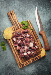 Cooked octopus pieces, fresh lemon slices, and parsley on a rustic wooden cutting board, preparing...