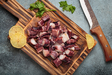 Cooked octopus pieces, fresh lemon slices, and parsley on a rustic wooden cutting board, preparing seafood for a healthy meal