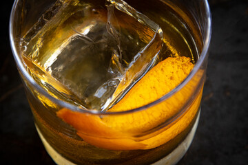 Close up of an orange peel in an old fashioned drink with a large ice cube