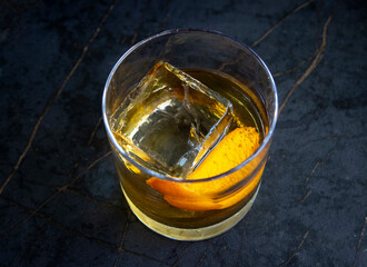 Close up and full shot of an orange peel in an old fashioned drink with a large ice cube