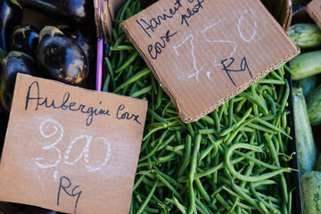 Fresh green beans displayed in a market with handwritten cardboard labels, including “Aubergine corx” and a price.